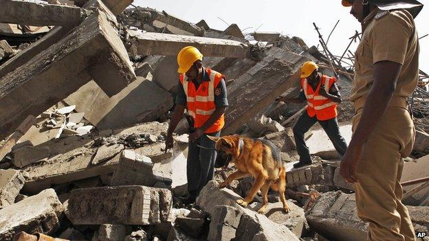 Rescuers with a sniffer dog search for workers believed buried in the rubble of a building that collapsed late Saturday during monsoon rains on the outskirts of Chennai, India, Sunday, June 29