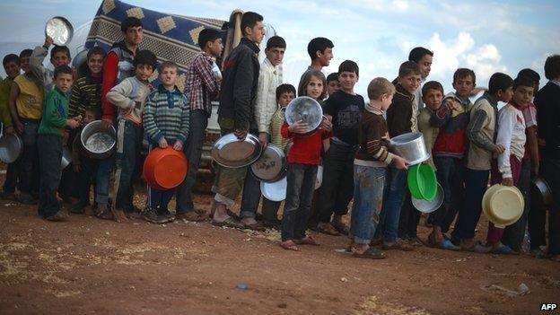 Internally displaced Syrian youths hold empty pots as they line up for food distribution