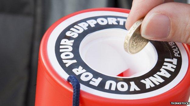Somebody putting a pound coin into a charity tin