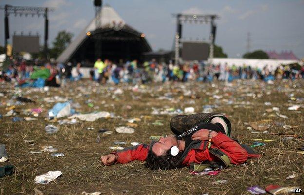 Man asleep in front of the Pyramid Stage surrounded by lots of rubbish