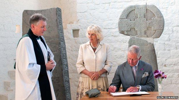 The Prince signs the visitors’ book at St Illtud’s Church at Rev Huw Butler talks to the Duchess of Cornwall