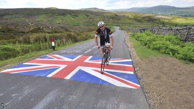 A rider passes over a Union flag painted on the road on the moors above Leyburn with the Yorkshire Dales in the background