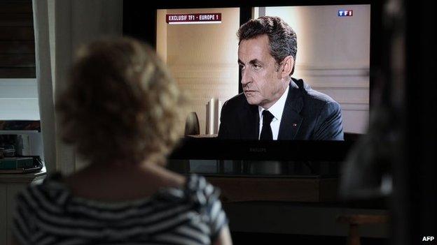 A woman watches a televised interview with former French President Nicolas Sarkozy