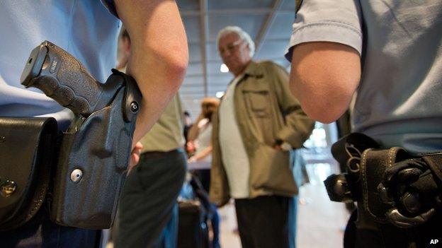 Police guards as passengers queue at the security checkpoint at the Rhein-Main airport in Frankfurt, Germany, Thursday July 3