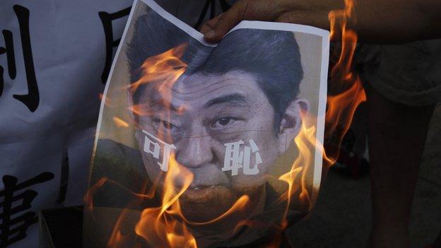 A protester burns a portrait of Japanese Prime Minister Shinzo Abe, with the Chinese characters "Shameful" written on it, outside the Japanese Consulate in Hong Kong on 7 July, 2014