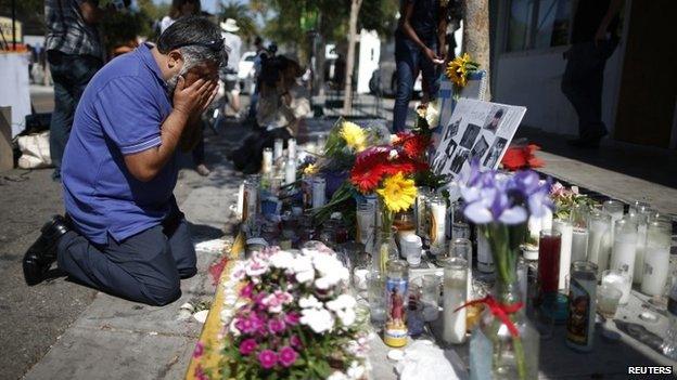 A man in Isla Vista kneels in front of a memorial to the victims