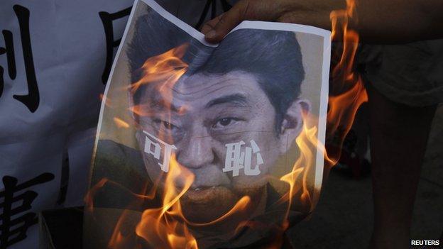 A protester burns a portrait of Japanese Prime Minister Shinzo Abe, with the Chinese characters "Shameful" written on it, outside the Japanese Consulate in Hong Kong on 7 July, 2014