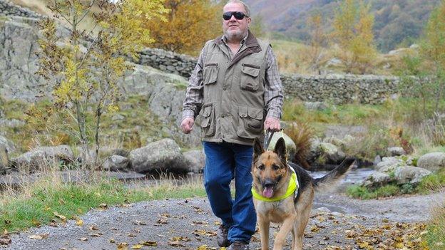 A blind man and his guide dog walking down a rural path in the countryside