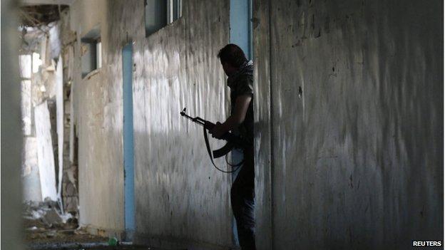 A man emerges from a doorway holding a gun in a damaged building