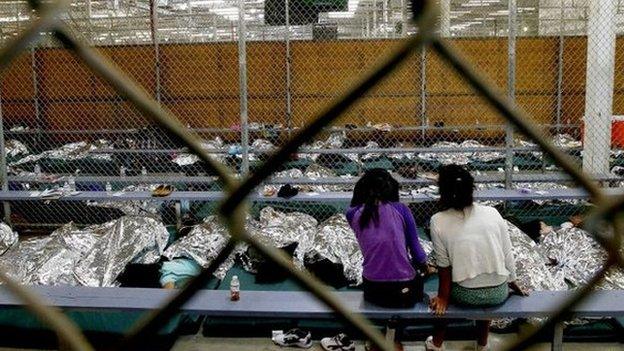 Two young girls watch a World Cup soccer match on a television from their holding area where hundreds of mostly Central American immigrant children are being processed and held at the US Customs and Border Protection Nogales Placement Center in Nogales, Arizona 18 June 2014