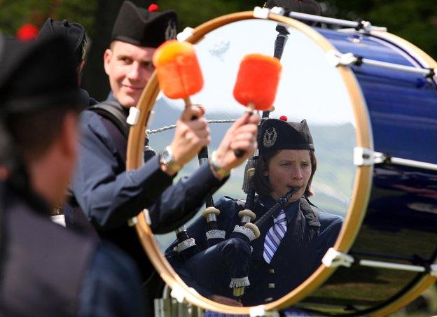 A female member of the pipe band of Corby is reflected in a drum as she plays the bagpipes