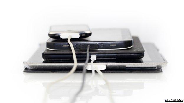 A stack of electronic items with charger wires attached