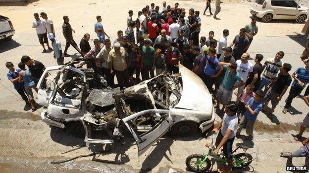 Palestinians gather around the remains of a car which police said was targeted in an Israeli air strike in the northern Gaza Strip on 10 July 2014.