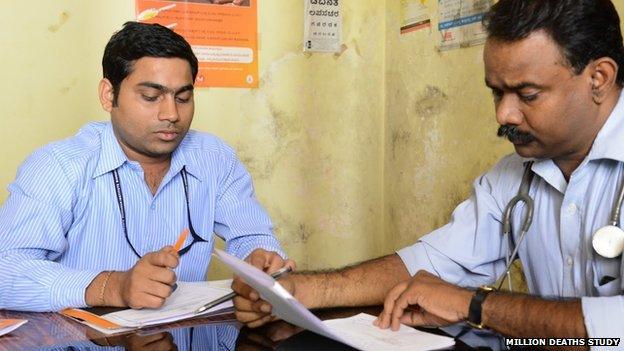 Two men sitting reading papers, one with stethoscope round his neck