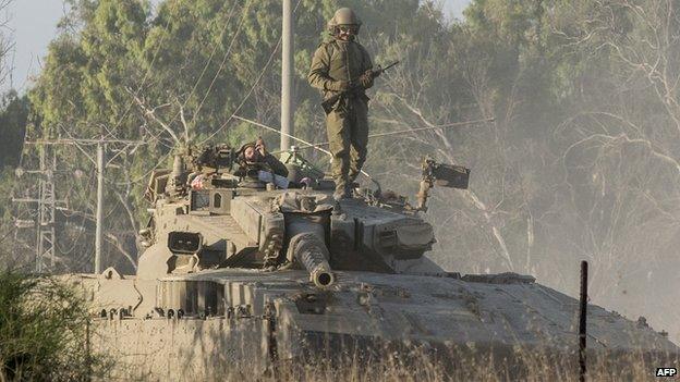 An Israeli soldier stands on his Merkava tank positioned along the southern Israeli border with the Gaza Strip following Israeli air strikes on 10 July 2014