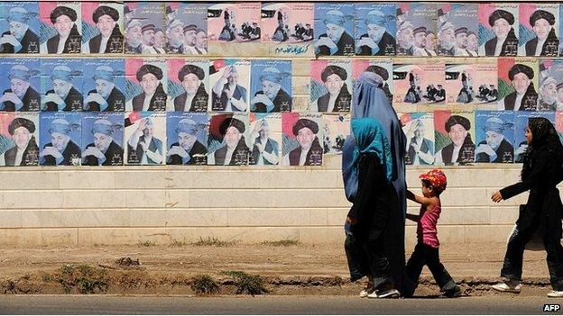 A burqa-clad Afghan woman with her children walk past a wall adorned with posters of Afghan President Hamid Karzai one of 41 presidential candidates in Herat on August 7, 2009.