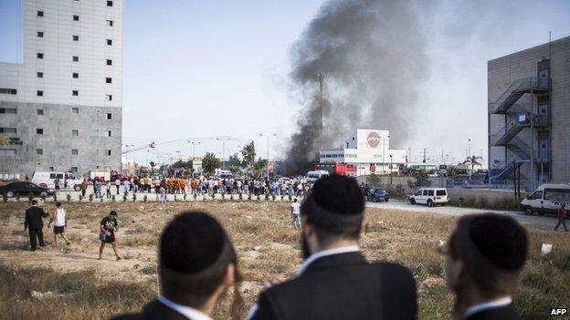 People watch as fire-fighters try to douse a fire from a rocket that hit a Petrol station on 11 July 2014 in Ashdod, Israel.