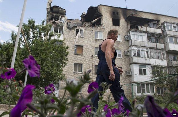 A man passes a damaged block of flats in Marinka, Donetsk, 12 July