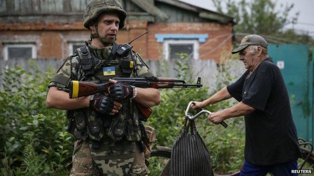 A local resident pushes a bicycle past a Ukrainian soldier in the eastern Ukrainian village of Semenivka, near Sloviansk. Photo: 14 July 2014