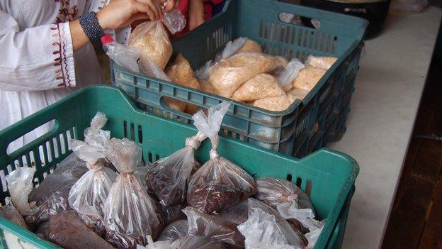 A woman ties up bags with rice as bags with beans lie ready