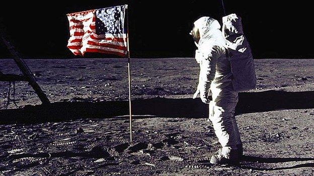 Buzz Aldrin stands near a US flag on the surface of the moon.