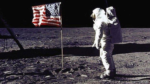 Buzz Aldrin stands near a US flag on the surface of the moon.