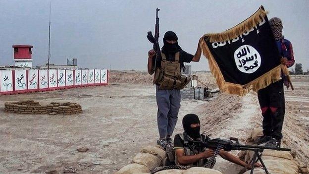 Isis fighters hold their flag aloft after taking control of an army checkpoint in the north of the country - 11 June 2014