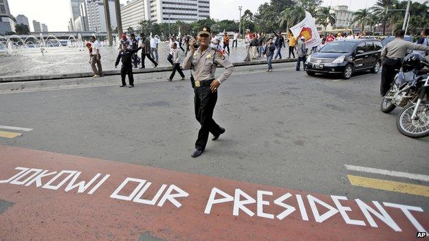 A police officer walks past a message taped on the road by supporters of presidential candidate Joko Widodo, during a rally in Jakarta, Indonesia on Thursday, 10 July, 2014