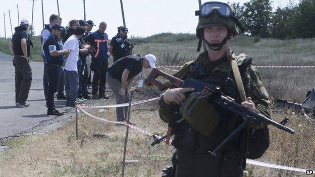 International investigators at the MH17 crash site guarded by an armed rebel in Donetsk, Ukraine (21 July 2014)