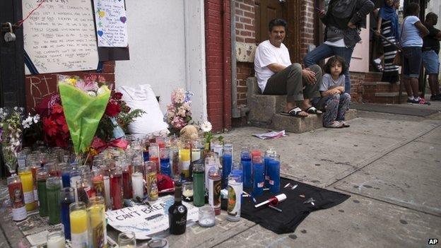 Pedestrians sit near a memorial for Eric Garner erected near the site of his death in New York on 19 July 2014