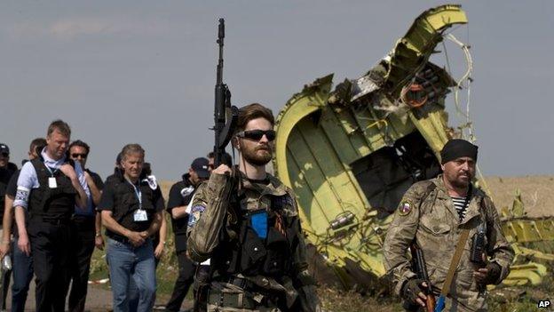 A pro-Russian rebel holds a gun passing by plane wreckage as members of the OSCE mission to Ukraine arrive for a media briefing at the crash site of MH17, July 22