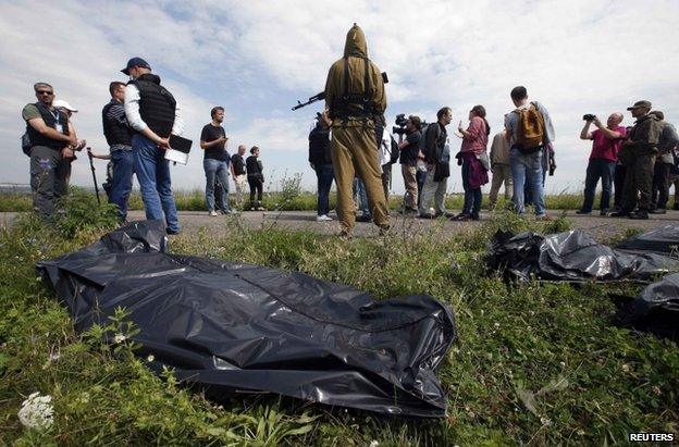 OSCE monitors, journalists and rebel fighters stand near recovered MH17 bodies in east Ukraine, 19 July