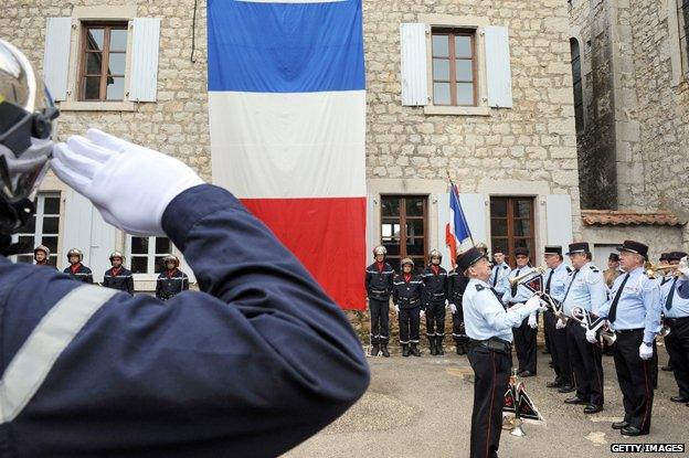 French officer salutes French flag while police and fire workers stand to attention