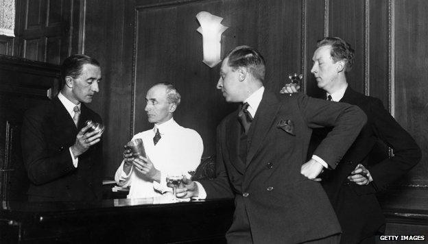 November 1927: Writers and brothers Osbert (1892 - 1969) and Sacheverell Sitwell (1897 - 1988) watch Martyn Roland of the Savoy Hotel and Harry Craddock the barman demonstrate how to shake a cocktail