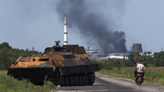 People ride a scooter past a destroyed military vehicle near the city of Lisichansk, Luhansk region, eastern Ukraine