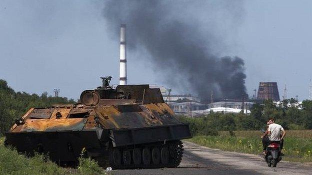 People ride a scooter past a destroyed military vehicle near the city of Lisichansk, Luhansk region, eastern Ukraine