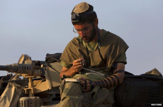 An Israeli soldier prays on top of a tank near the Gaza border, 29 July