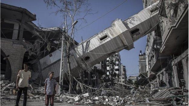 Palestinians walk next to the collapsed minaret of a mosque in Gaza City, 30 July 2014