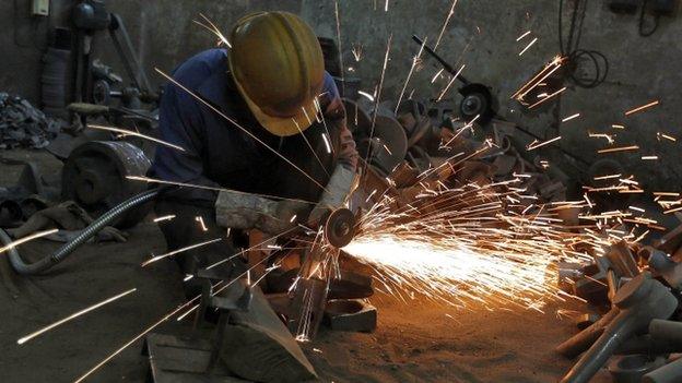 A worker grinds a metal shaft metal used in water pumps at a manufacturing unit