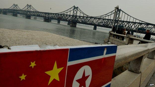 The Chinese and North Korean flags attached to a railing as trucks carrying Chinese-made goods cross into North Korea on the Sino-Korean Friendship Bridge at the Chinese border town of Dandong on 18 December 2013