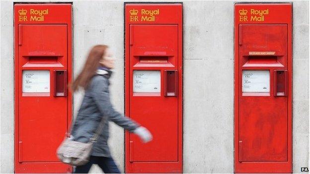 A woman walking past a Royal Mail post office