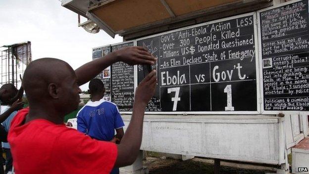 Liberians read the Daily Talk chalk board on the Ebola outbreak situation in Monrovia, 9 August 2014