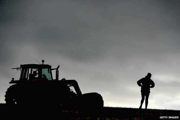 Scottish farmer silhouetted against horizon next to tractor