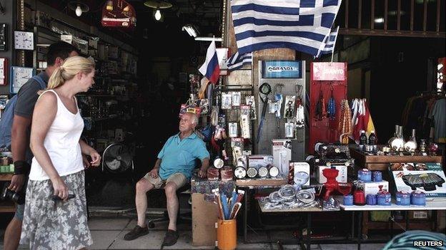 A shop owner looks at tourists walking by his shop in Athens - 13 August 2014