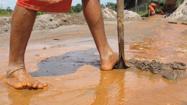 close up of man's bare legs and feet in brown water, digging the mine