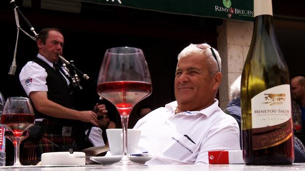 A glass of wine at a table with a bagpipe-playing man behind