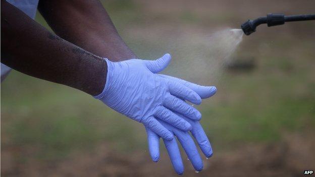 A Liberian burial team carefully disinfects their protective gloves for disposal after retrieving the body of an Ebola victim from his home on 17 August 2014 near Monrovia, Liberia