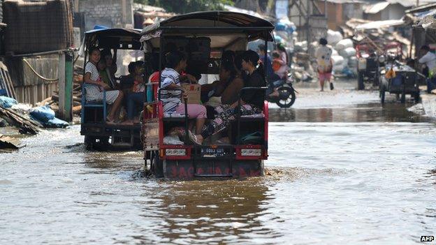 Residents of the Muara Angke fisherman village travel in three-wheel motor vehicles through water in the street from recent rains