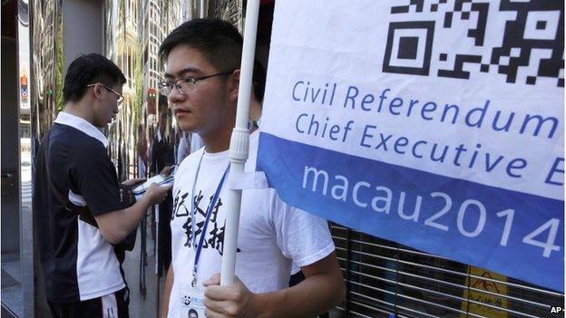 A man, left, votes on a tablet next to a volunteer with a banner promoting informal civil referendum in a street of the former Portuguese colony, Macau, Sunday, 24 Aug 2014.