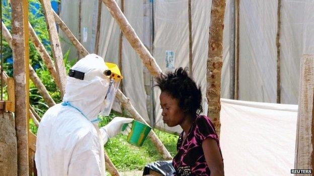 A health worker offers water to a woman with Ebola in Kenema, Sierra Leone, in July 2014.